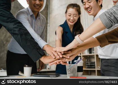 Asian businessmen and businesswomen meeting brainstorming putting hands up for new startup and giving strength motivation working together in modern creative office. Coworker teamwork concept.