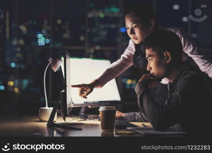 Asian businesswoman and businessman working hard late together with technology computer in office, customer service and call center, team work with colleagues for success achievement project concept