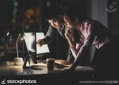 Asian businesswoman and businessman working hard late together with technology computer in office, customer service and call center, team work with colleagues for success achievement project concept