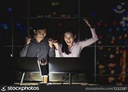 Asian businesswoman and businessman working hard late together with technology computer in office,team work with colleagues to congratulations for success achievement project concept