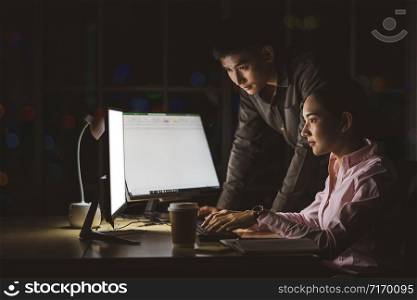 Asian businesswoman and businessman working hard late together with technology computer in office, customer service and call center, team work with colleagues for success achievement project concept