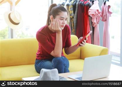 Asian businesswoman blogger sitting on yellow sofa and hand holding taplet with serios for checking sale down in online shopping on website. Marketing in social media concept.