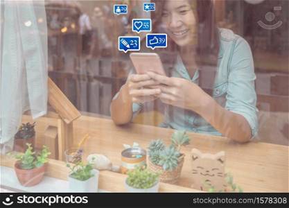 Asian businesswoman hand using the smart mobile phone for social netwrok media with number of Like, Love, comment, people and fovorite icon in modern coffee shop beside window, Social network concept