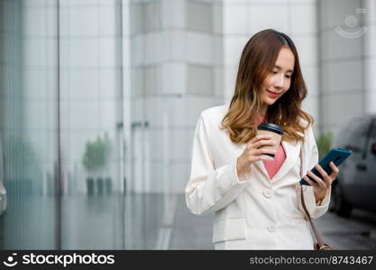 Asian businesswoman holding coffee cup takeaway look smartphone going to work walk on city street near office in morning, Portrait business woman hold mobile phone and paper cup of hot drink outdoor