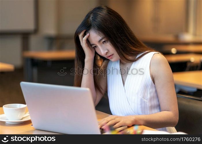 Asian businesswoman in casual suit looking at annual report and thinking with serious action in modern office, business failure, healthcare and office syndrome concept