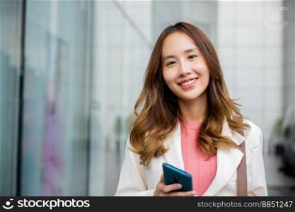 Asian businesswoman texting smartphone commuting work she walking near her office building, Happy business woman smiling using mobile phone outdoor walking on city street urban looking to camera