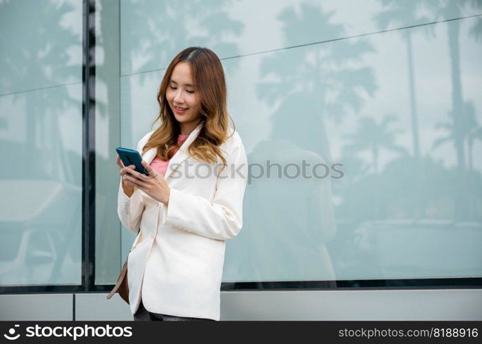 Asian businesswoman typing text on mobile phone standing outdoors street front building near office, Portrait successful business woman smiling holding smartphone using app chat online in morning