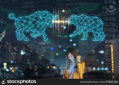 Asian businesswoman using smart mobile phone with smile action showing Bull and Bear polygonal shape writing by lines and dots over Stock market exchange and Trading graph on the cityscape background