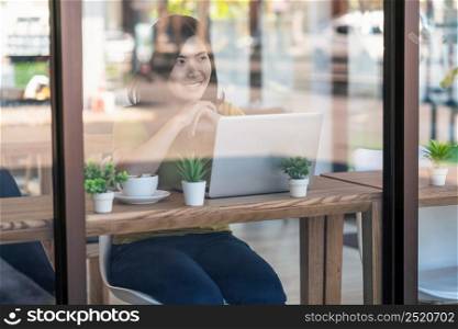 Asian businesswoman working from home with technology laptop computer in happiness feeling at desk beside the glass in modern coffee shop or office,Business owner and entrepreneur concept