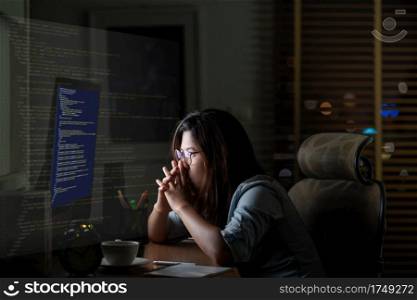 Asian Businesswoman working hard with front of computer desktop with programming source code and motion graphic over computer screen in work place at late times with exciting and serious action