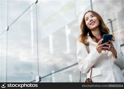 Asian businesswoman working with mobile phone standing against street front building near office, Portrait successful business woman smiling holding smartphone use application chat online in morning