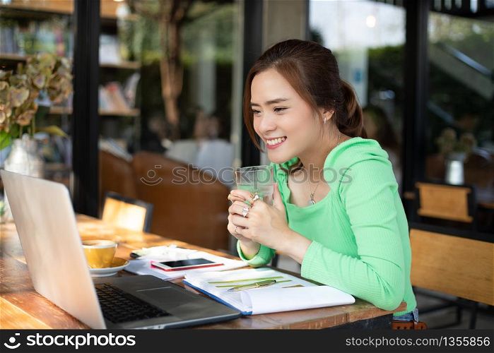 Asian businesswomen smiling and using notebook for analysis documents and graph financial diagram working and she is holding glass of water for drinking