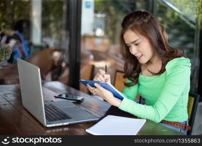 Asian businesswomen smiling and using notebook for analysis documents and graph financial diagram working and she is drinking coffee