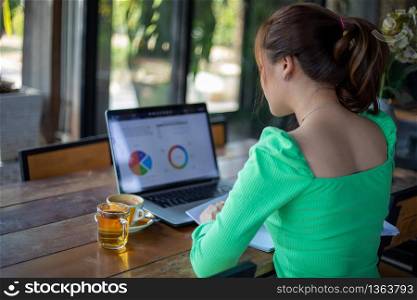 Asian businesswomen smiling and using notebook for analysis documents and graph financial diagram working and she is drinking coffee at coffee shop