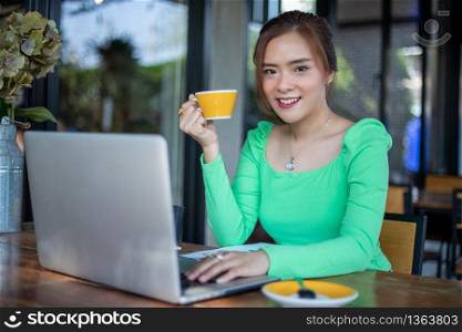 Asian businesswomen smiling and using notebook for analysis documents and graph financial diagram working and she is drinking coffee at coffee shop