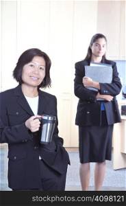 Asian Businesswomen with coffee Mug and assistant in background - focus on front woman