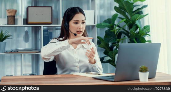 Asian call center with headset and microphone working on her laptop. Female operator provide exceptional customer service. Supportive call center agent helping customer on inquiry. Enthusiastic. Enthusiastic asian call center with headset and microphone working on her laptop