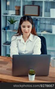 Asian call center with headset and microphone working on her laptop. Female operator provide exceptional customer service. Supportive call center agent helping customer on inquiry. Enthusiastic. Enthusiastic asian call center with headset and microphone working on her laptop