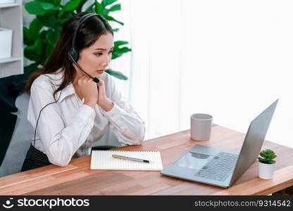 Asian call center with headset and microphone working on her laptop. Female operator provide exceptional customer service. Supportive call center agent helping customer on inquiry. Enthusiastic. Enthusiastic asian call center with headset and microphone working on her laptop