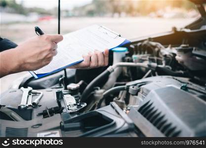 Asian car mechanic doing a check list and note report on paper clipboard.