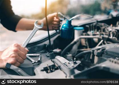 Asian car mechanic holds a wrench and a bottle of lure oil, ready to repair the car.
