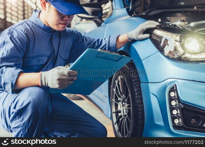 Asian car mechanic technician holding clipboard and checking to maintenance vehicle by customer claim order in auto repair shop garage. Wheel tire repair service. People occupation and business job