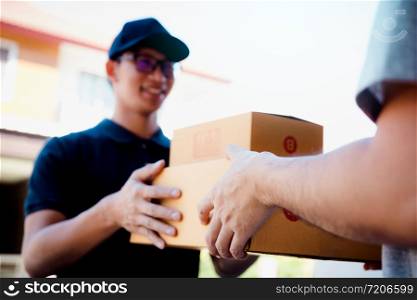 Asian cargo carrier holds a cardboard box with the package inside and the recipient is signing the package.