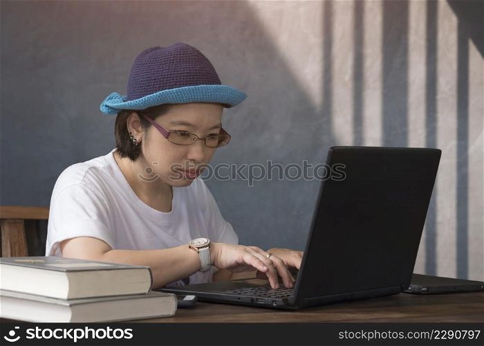 Asian casual woman using laptop computer on wooden desk while work from home in vintage living room