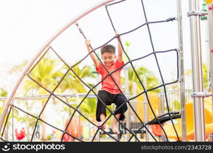 Asian child smiling playing climbing outdoor playground, happy preschool little kid having funny while playing climbs on a rope climbing net on playground equipment in daytime in summer, Little boy