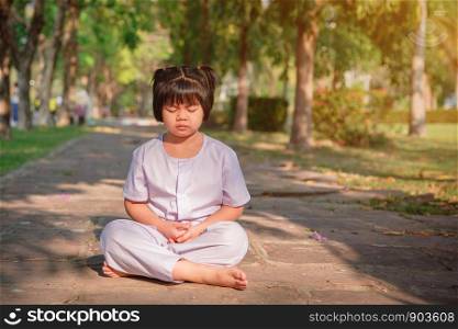Asian children cute or kid girl sit for meditation with peace and relax in garden pavilion at temple or church and wearing white dress with sunlight on white with space