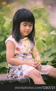 asian children sitting in garden with yellow cosmos flower in hand