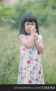asian children use hand close her nose standing in green garden