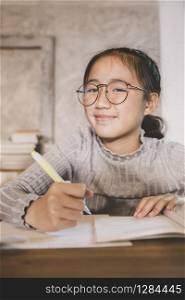 asian children wearing eye glasses with pen in hand studying in home living room