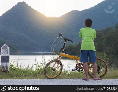 Asian children with yellow bicycle seeing sunset with mountain