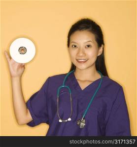 Asian Chinese mid-adult female doctor holding holding up CD against yellow background smiling and looking at viewer.