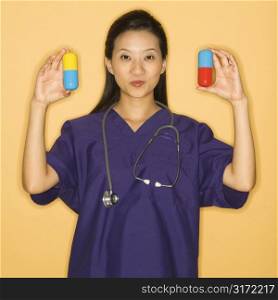 Asian Chinese mid-adult female doctor holding up giant pills against yellow background smiling and looking at viewer.