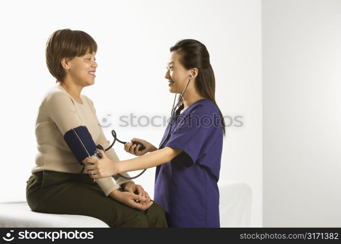 Asian Chinese mid-adult female medical practitioner checking blood pressure of African American middle-aged female patient.