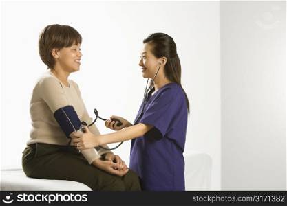Asian Chinese mid-adult female medical practitioner checking blood pressure of African American middle-aged female patient.