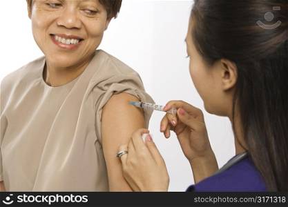 Asian Chinese mid-adult female medical practitioner giving shot in arm of African American middle-aged female patient.