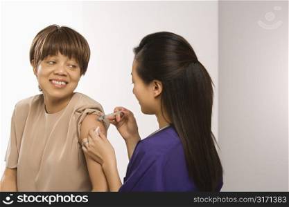 Asian Chinese mid-adult female medical practitioner giving shot in arm of African American middle-aged female patient.