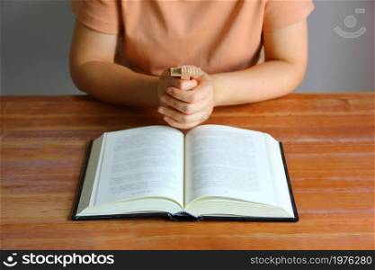Asian Christain woman praying while holding wood cross in front of the bible