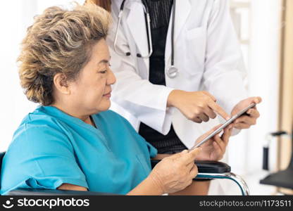 Asian confidence doctor using digital tablet expressing health concerns with old elderly woman patient sit on wheelchair