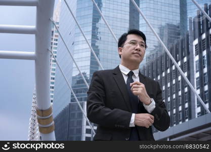 Asian confident Businessman standing in suit and looking away with modern city background