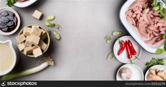 Asian cooking ingredients in bowls with tofu, chili, soy sauce, meat, ginger and broth on gray concrete background, top view, banner. Asian cuisine concept