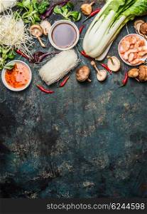 Asian cooking ingredients: rice noodles, pok choy , sauces, shrimps, chili and Shiitake mushrooms on dark background, top view, place for text. Asian food concept: Chinese or Thai cuisine.