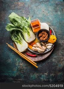 Asian cooking ingredients with pak choi , ginger, spices, chili and chopsticks on wooden dish for Chinese or Thai cuisine on dark rustic background, top view