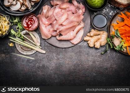 Asian cooking preparation with ingredients : chicken Strips, Shoots, vegetables and spices on dark rustic background, top view, border