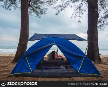 Asian couple camping on beach and resting in front of the tent with sea background.