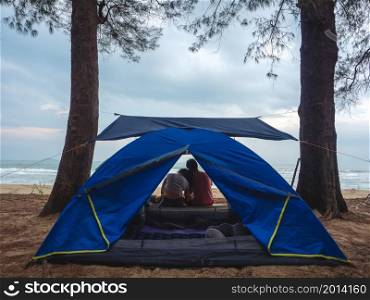 Asian couple camping on beach and resting in front of the tent with sea background.