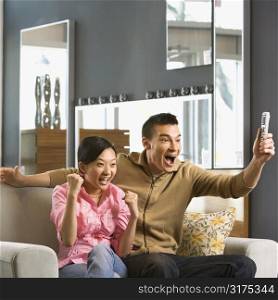 Asian couple cheering while watching television.